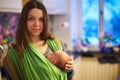 Young woman with newborn infant baby in a sling with a blurred background at home Royalty Free Stock Photo