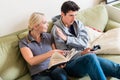 Young woman reading a book next to her boyfriend watching TV Royalty Free Stock Photo