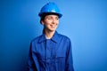 Young beautiful worker woman with blue eyes wearing security helmet and uniform looking away to side with smile on face, natural Royalty Free Stock Photo