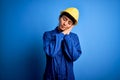 Young beautiful worker woman with blue eyes wearing security helmet and uniform sleeping tired dreaming and posing with hands