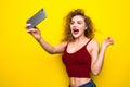 Young beautifulgirl with an curly hairstyle. Laughing girl take selfie from phone on Yellow background.