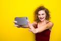 Young beautifulgirl with an curly hairstyle. Laughing girl take selfie from phone on Yellow background.