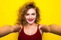 Young beautifulgirl with an curly hairstyle. Laughing girl take selfie from phone on Yellow background.