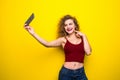 Young beautifulgirl with an curly hairstyle. Laughing girl take selfie from phone on Yellow background.