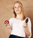 Young beauty blond teenage girl eating chocolate smiling, choice between sweet and apple Royalty Free Stock Photo