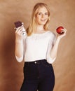 Young beauty blond teenage girl eating chocolate smiling, choice between sweet and apple Royalty Free Stock Photo