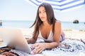 Young beauty latin woman lying under sun umbrella and working on her laptop on the beach. Summer vocation Royalty Free Stock Photo