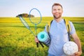 A young beauty man on picnic with backpack, rackets for badbotton and ball smiles against background of a green meadow Royalty Free Stock Photo