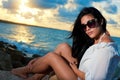 Young beauty with sunglasses sitting on a rock by the ocean Royalty Free Stock Photo