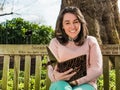 Young Beauty Woman Reading Book and Smiling Seated on Park Bench