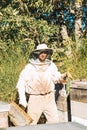 Young beekeeper with special suit transporting honeycomb completely closed in the middle of the beehives