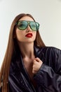 Young beutiful brunnette girl posing in green suglasses and black leather jacket posing over grey studio backgorund Royalty Free Stock Photo