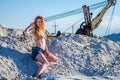 Young bewitching girl with long beautiful hair in denim shorts and a bikini bathing suit sitting on a mountain of sand in the Royalty Free Stock Photo