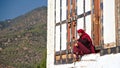 A monk sitting on the porch to a house and checking his mobile phone in Bhutan