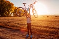 Young bicyclist raising her bicycle in autumn field. Happy woman celebrates success holding bike in hands Royalty Free Stock Photo