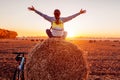 Young bicyclist sitting on haystack with raised and opened arms after a ride. Woman having rest in autumn field. Royalty Free Stock Photo