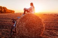 Young bicyclist sitting on haystack after a ride. Woman having rest in autumn field. Sportive lifestyle Royalty Free Stock Photo