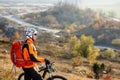 Young bicyclist standing near and looking to mountains