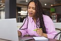 Young biracial woman with long braided hair working on laptop in a modern business office Royalty Free Stock Photo