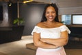 A young biracial woman is standing with arms crossed, smiling, in a modern business office with copy Royalty Free Stock Photo