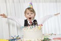 Young birthday wearing party hat with arms outstretched blowing candles on cake Royalty Free Stock Photo