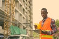 Young black African man construction worker reading on clipboard while holding hard hat at building site Royalty Free Stock Photo