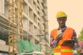 Young black African man construction worker reading on clipboard while holding mobile phone at building site Royalty Free Stock Photo