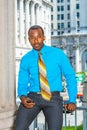 Young black businessman sitting outside office in New York City, texting on cell phone, thinking Royalty Free Stock Photo