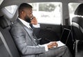 Young black businessman using mobile phone and laptop in car Royalty Free Stock Photo
