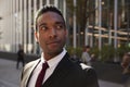 Young black businessman wearing black suit standing on the street smiling, looking away, close up Royalty Free Stock Photo