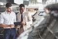 A young black businesswoman signs documents and buys a new car. The car dealer is standing next to him