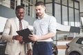 A young black businesswoman signs documents and buys a new car. The car dealer is standing next to him