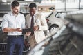 A young black businesswoman signs documents and buys a new car. The car dealer is standing next to him