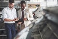 A young black businesswoman signs documents and buys a new car. The car dealer is standing next to him