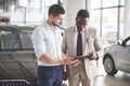 A young black businesswoman signs documents and buys a new car. The car dealer is standing next to him