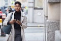 Young black businesswoman walking in the street in London using her smartphone, front view