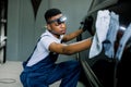 Young black car wash worker man, wearing protective clothes and gloves, cleaning modern black car with microfiber cloth Royalty Free Stock Photo