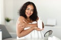 Young black chubby lady applying moisturizing body lotion on shoulder, using nourishing cream for skin Royalty Free Stock Photo