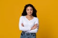 Young black confident lady posing with folded arms over yellow background