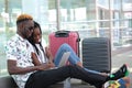 Young black couple checking their travel schedule on a laptop, sitting at the station with their suitcases