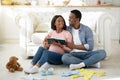 Young black couple expecting baby and writing checklist of child stuff for maternity hospital, sitting on floor at home Royalty Free Stock Photo