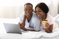 Young black couple laying on bed with laptop, shopping online