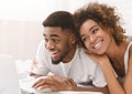 Young black couple lying on bed and using laptop. Royalty Free Stock Photo