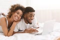 Young black couple lying on bed and using laptop. Royalty Free Stock Photo