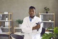 Young black doctor standing in medical office, holding stethoscope and looking at camera Royalty Free Stock Photo