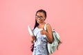 Young black female student with books and backpack showing thumb up gesture, smiling at camera over pink background Royalty Free Stock Photo
