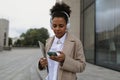 a young black female student in headphones with a mobile phone and a laptop walks around the city next to a modern Royalty Free Stock Photo