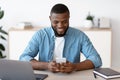 Young Black Freelancer Guy Sitting At Desk And Using Smartphone Royalty Free Stock Photo