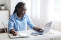 Young Black Freelancer Woman Working On Laptop At Home Office, Taking Notes