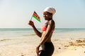 young black girl holds the Kenyan flag against the backdrop of a beautiful African beach.